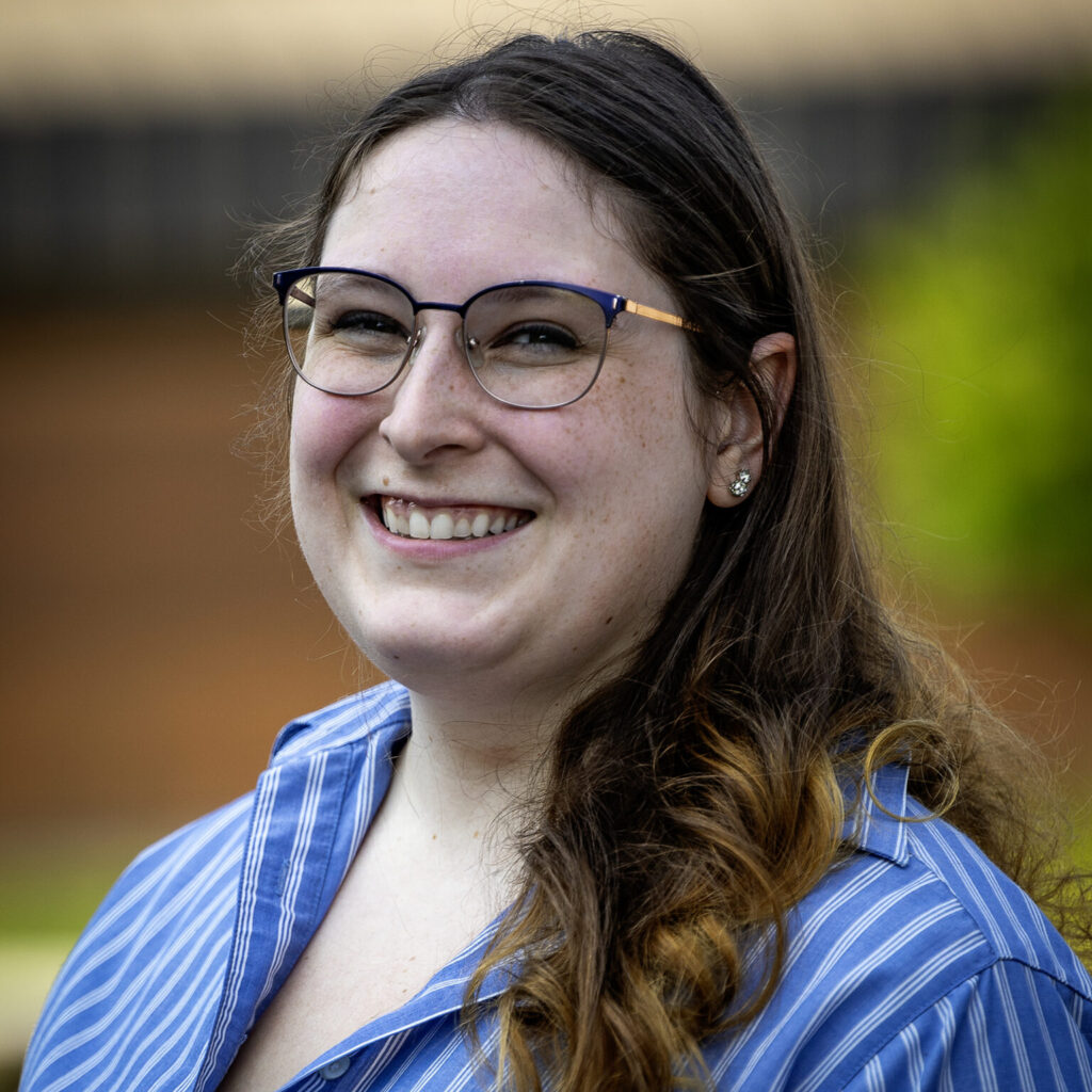 A woman in blue shirt in front of a blurred out background.