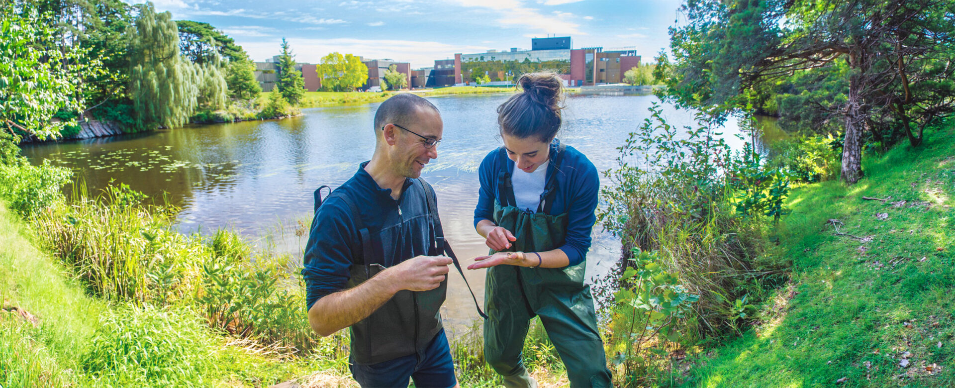 A man and woman looking at something in their palm with the lake and Nipissing building behind them