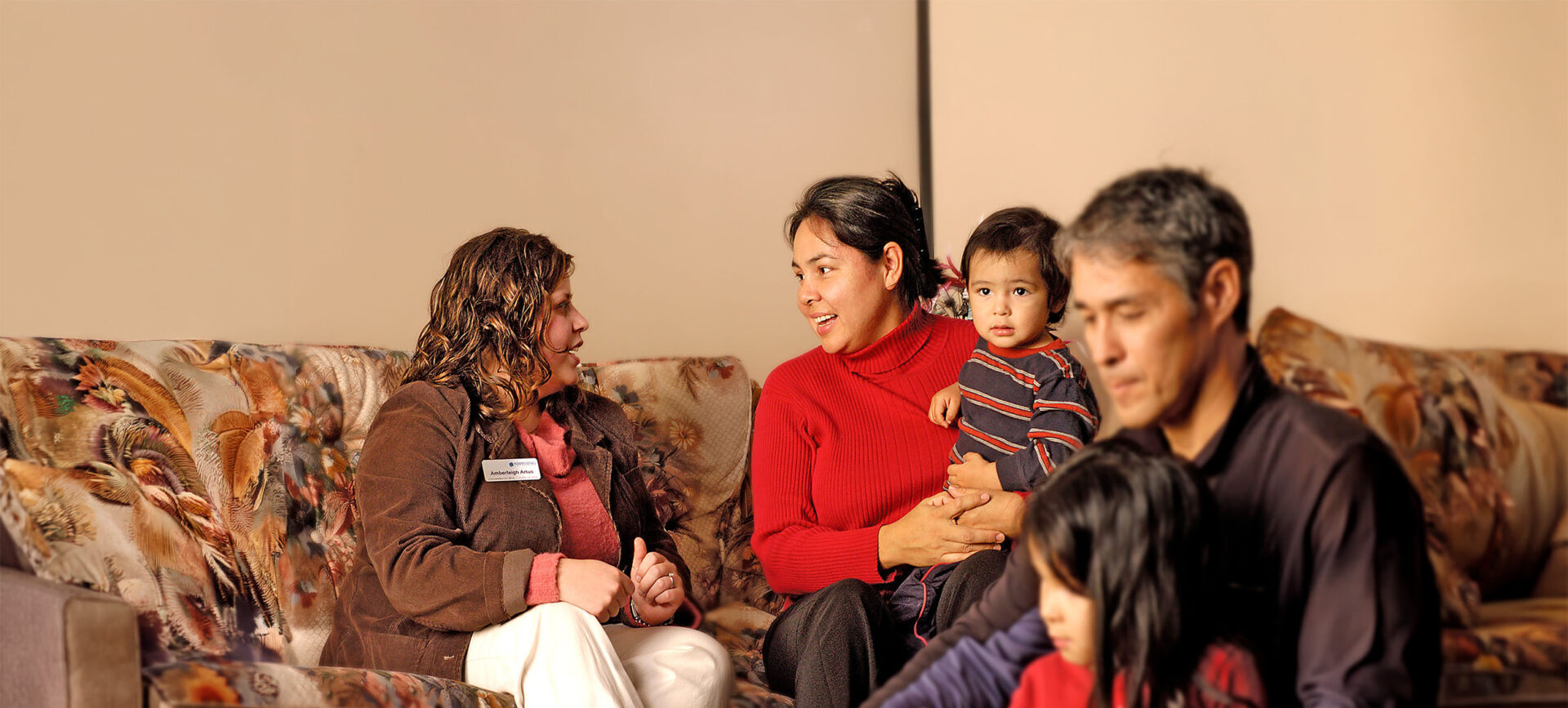 A Nipissing student talking to a mom in red holding her baby with the dad in front with their other child