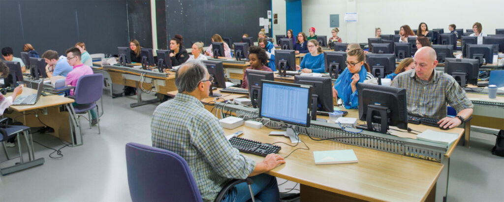 A classroom full of students looking at their monitor with the professor at the front