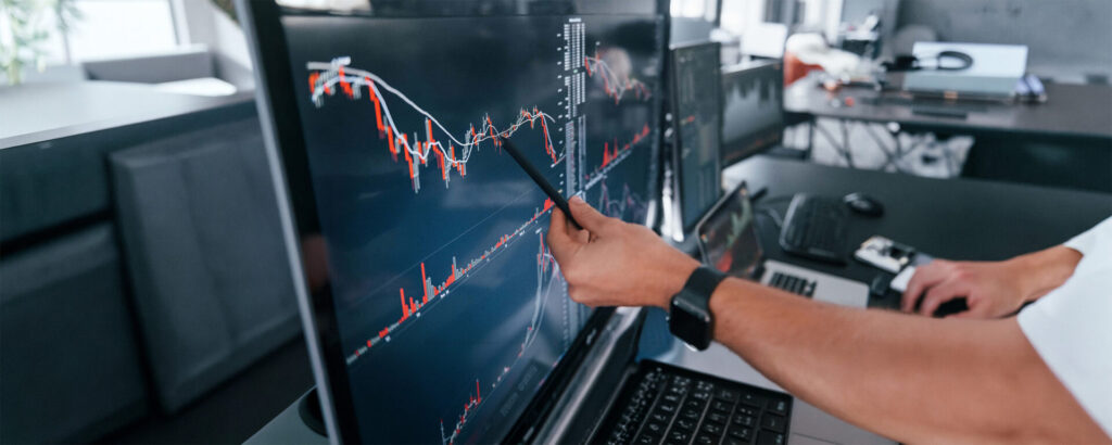 Someone's hand holding a pen pointing to a computer screen displaying red and blue data