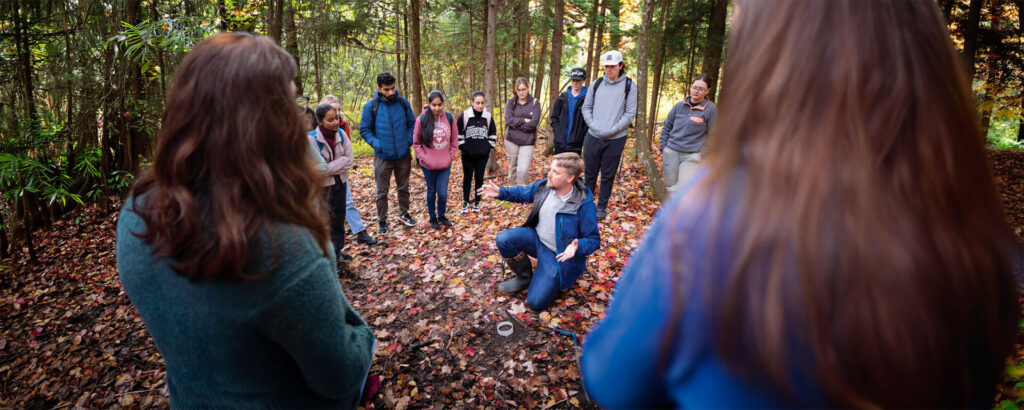 A group of students surrounding a professor giving a lecture in the trail