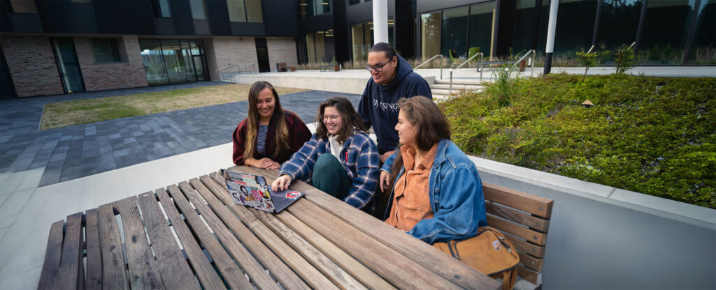 4 students sitting on a bench outside of the student centre