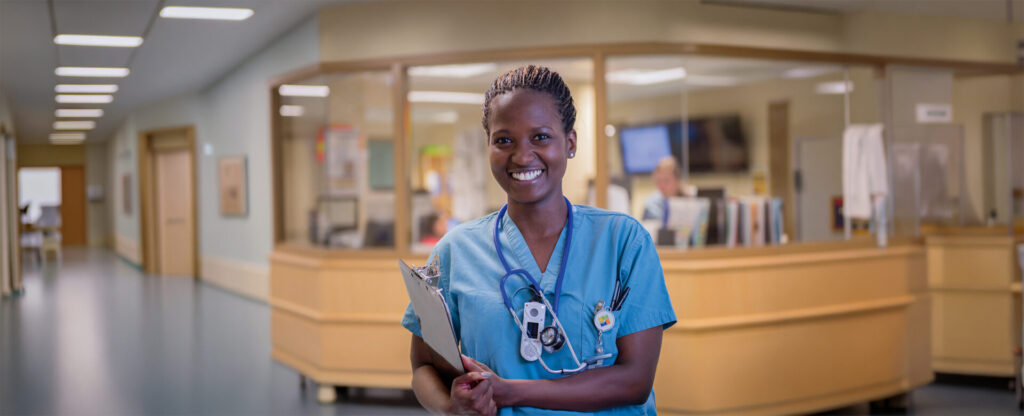 A female nurse holding her note pad with the hospital front desk in view behind her