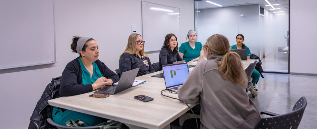 A group of nurses in scrubs working on their laptop in the nursing lab
