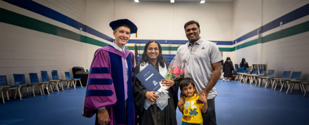 A graduate in convocation gown with her professor in purple gown and her husband and kid