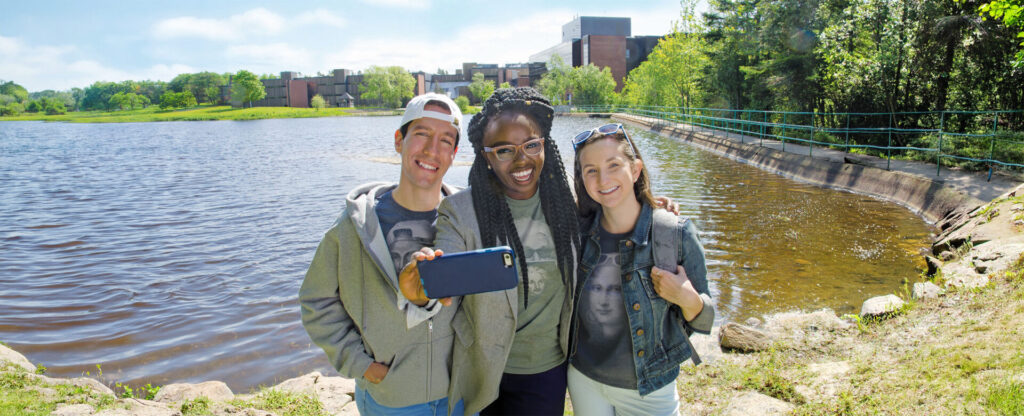 3 students taking a picture with Nipissing's pond as the background