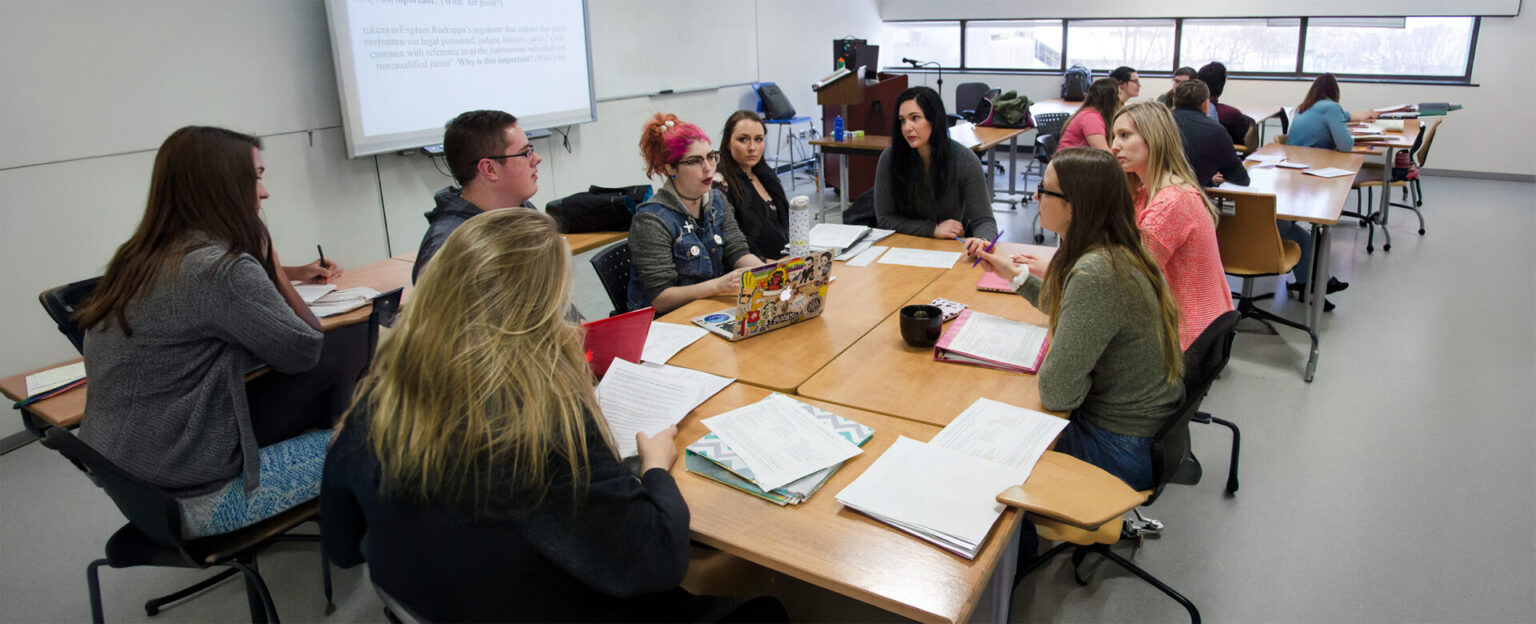 A group of students in a discussion with note books in front of them in a classroom setting