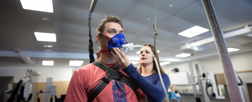 A student in red with a face mask put on him by a female student in navy blue top