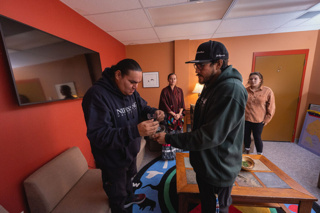 2 male students in green and blue hoodie performing an indigenous act in the sacred space