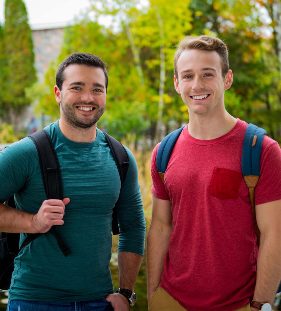 2 male students in green and red shirt standing outside with a nature background behind them