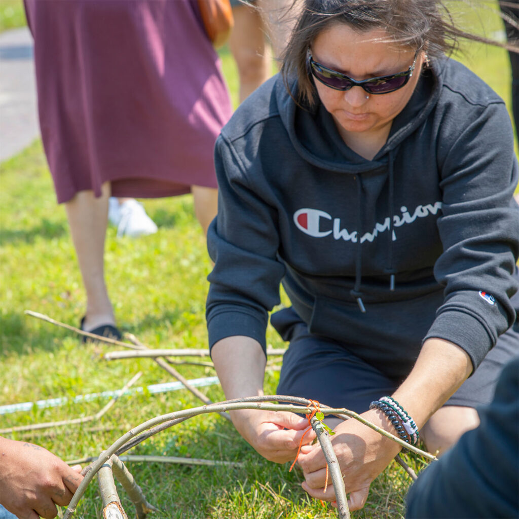 A woman making something out of thin twig in an outdoor setting