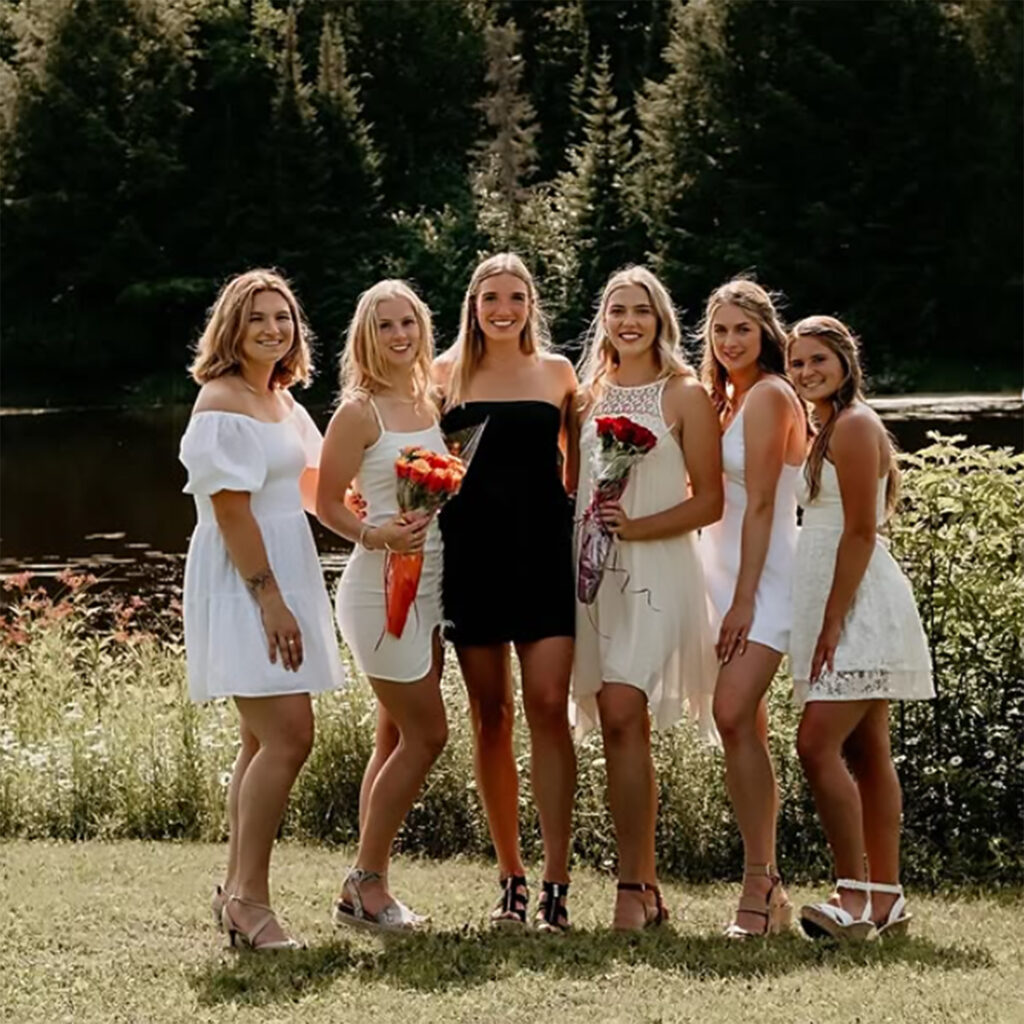 A group of nursing graduates in white and black dresses posing in front of a nature background