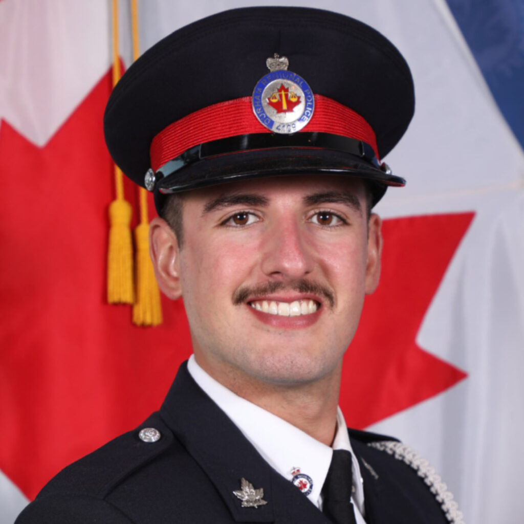 A Nipissing graduate in policing uniform in front of the Canadian flag