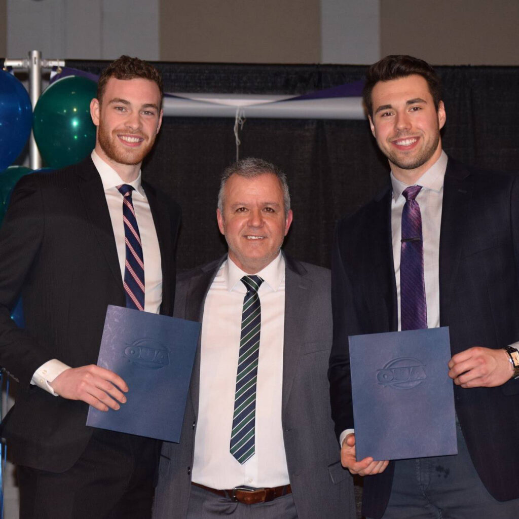2 graduates in suits holding their degree with a man in the middle