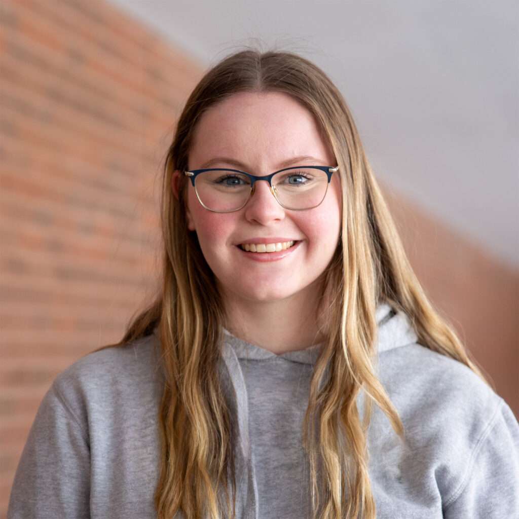A woman in grey hoodie against a brick background