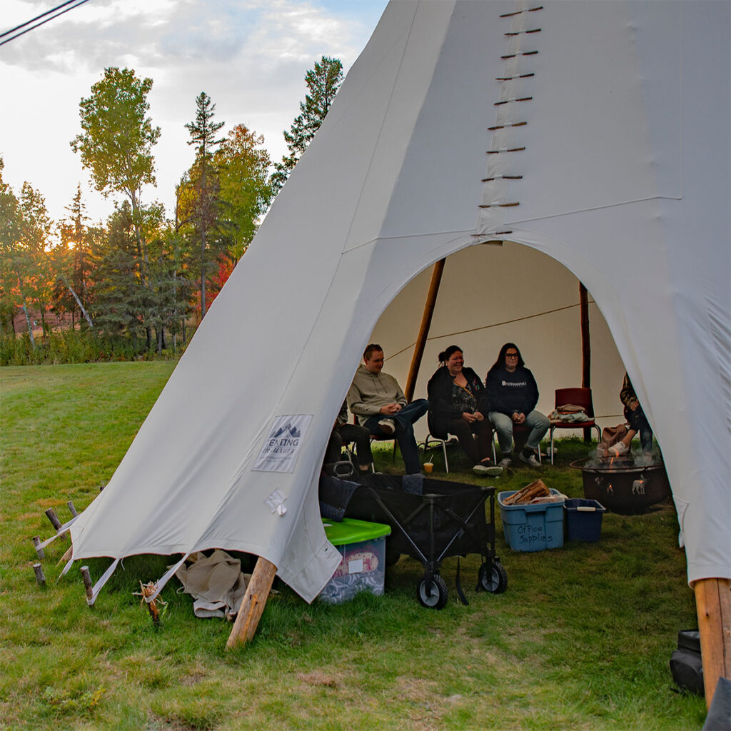 An outside view peeking into the tipi with people sitting around the fire