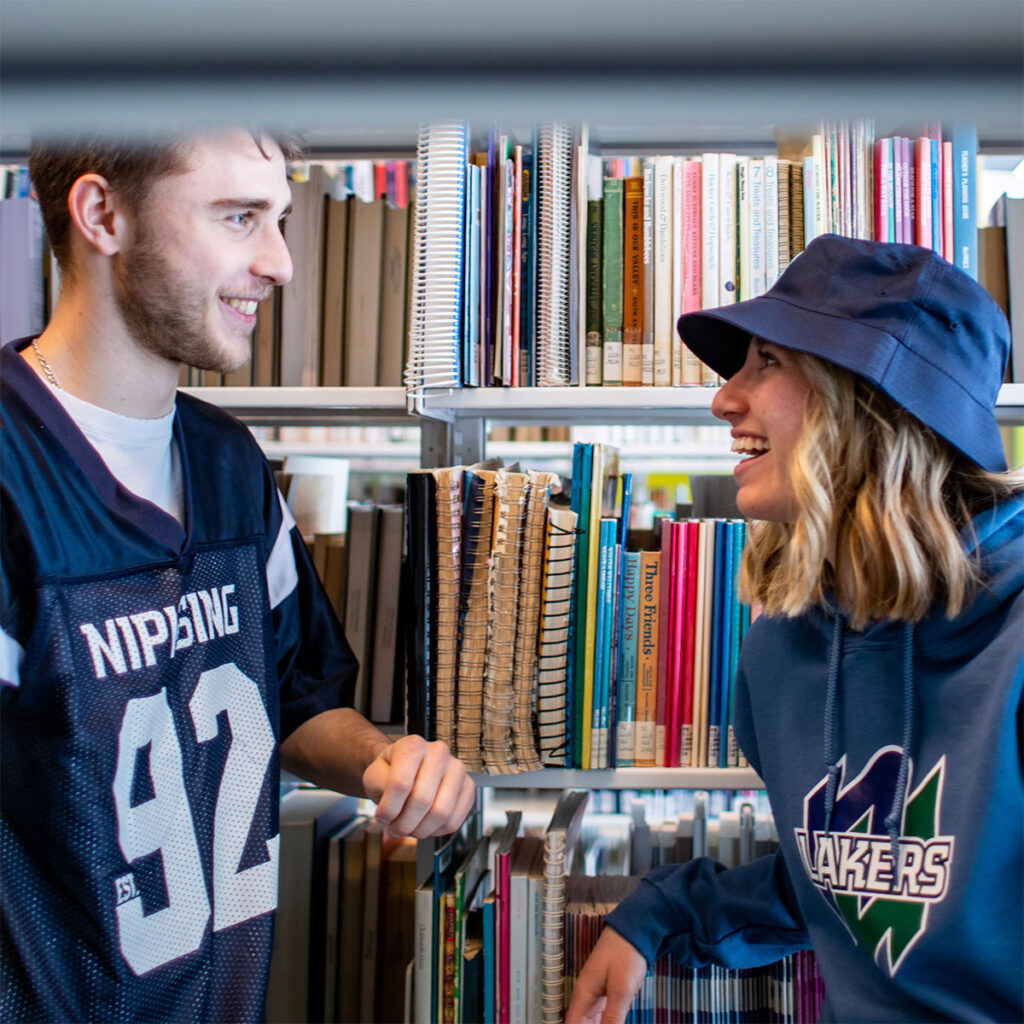 2 students talking and laughing between bookshelves in the library