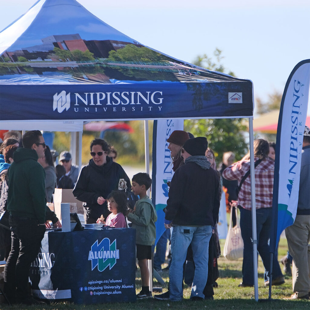 A Nipissing tent at an outdoor event with people chatting under it