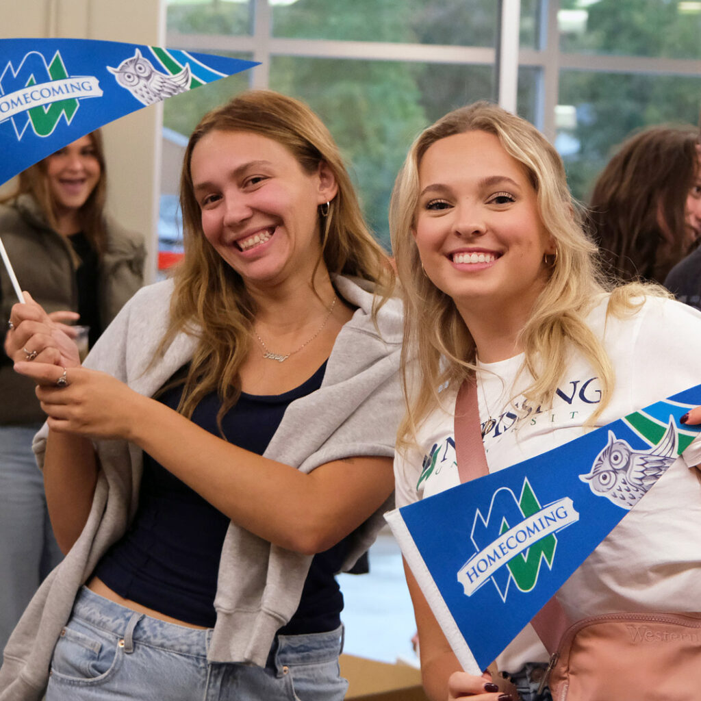 2 students holding homecoming flag and smiling