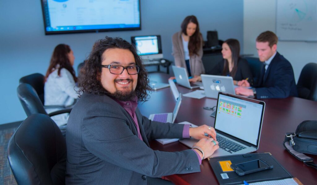 A man in suit working on his laptop with a group of people also working in the background