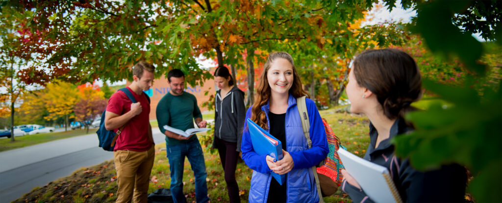 A group of students standing outside holding text books in a fall nature setting