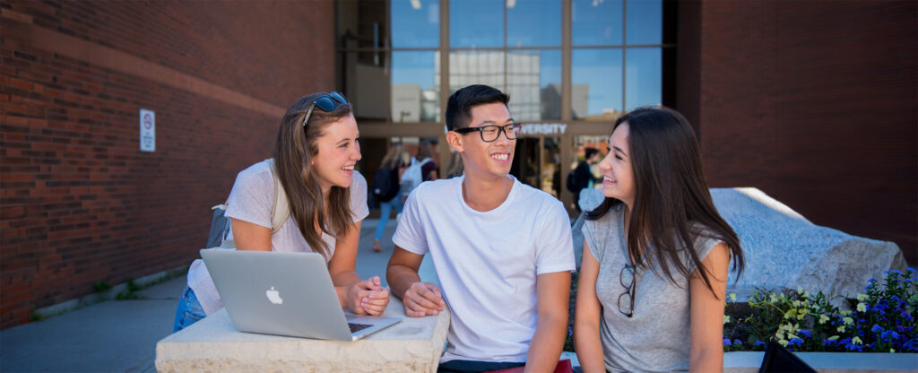 3 students sitting outside the university entrance
