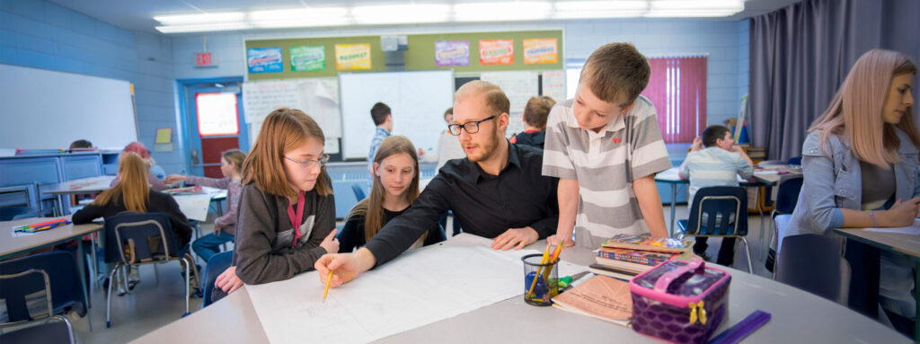 A teacher in black shirt sitting around a table with 3 students