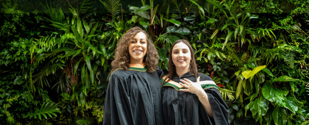 2 graduate students in black gown standing against a green nature background