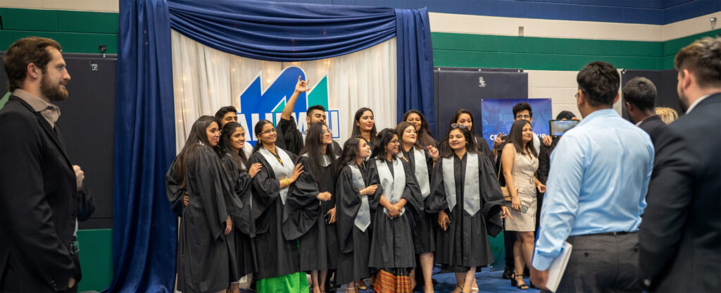 A group of graduate students posing for a photo in front of background with Nipissing workmark
